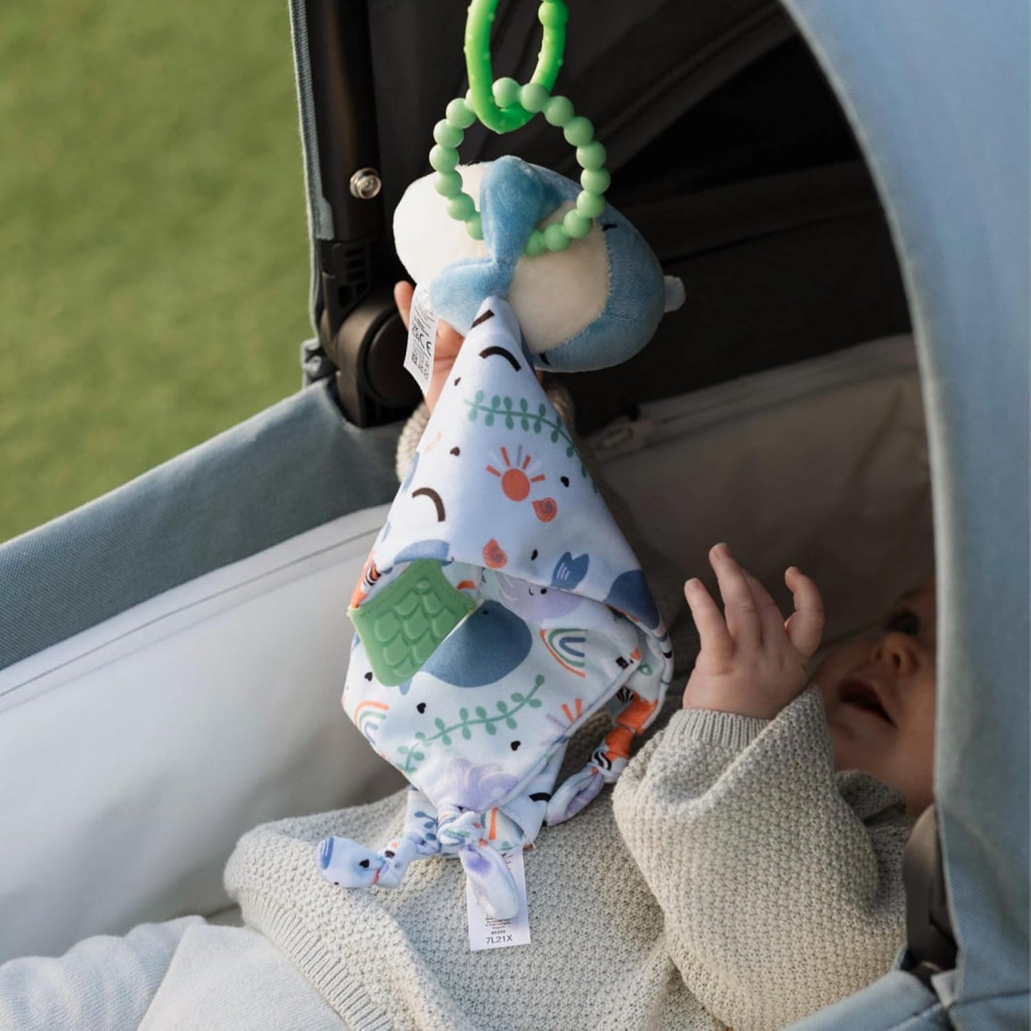 Baby playing with a colorful mobile toy hanging from a stroller.